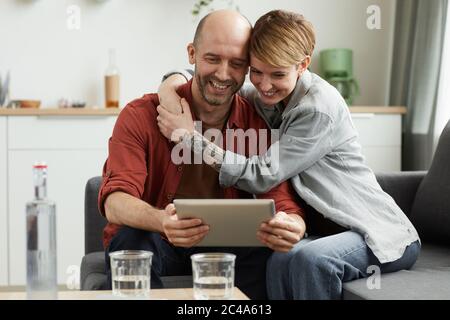 Young smiling couple sitting o sofa and looking at digital tablet they talking to their friends online at home Stock Photo