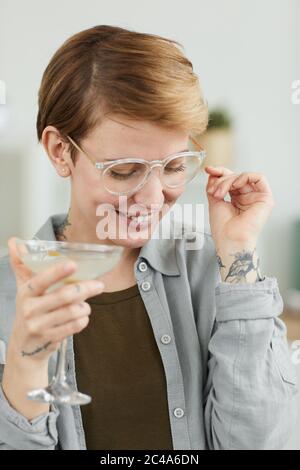 Young woman with short hair wearing eyeglasses holding alcohol drink and smiling Stock Photo