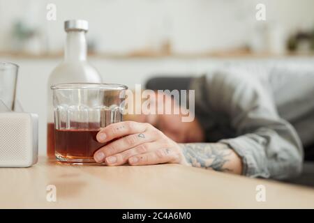 Glass of whiskey on the table with woman sleeping in the background she is in the kitchen at home Stock Photo
