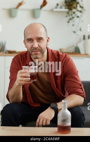 Portrait of mature man sitting on sofa with glass of whiskey and looking at camera he resting at home Stock Photo