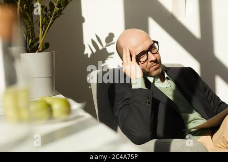 Mature businessman in eyeglasses sitting on chair and reading documents while working at office Stock Photo