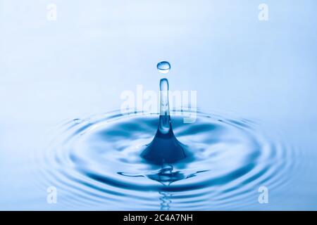 Water droplet falling impact with water surface. causing rings on water surface. Stock Photo