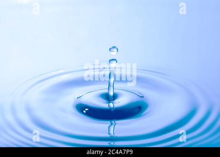 Water droplet falling impact with water surface. causing rings on water surface. Stock Photo
