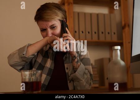 Young woman drinking alcohol and telling about her problems to somebody on mobile phone Stock Photo