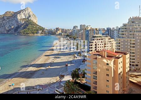 Sandy beach with parasols and vacationers, Penyal d'Ifac Natural Park view. Turquoise blue Sea water summer day. Seafront promenade of Calpe spanish r Stock Photo