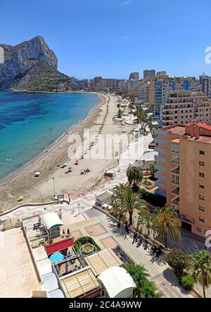 Sandy beach with parasols and vacationers, Penyal d'Ifac Natural Park view. Turquoise blue Sea water summer day. Seafront promenade of Calpe spanish r Stock Photo