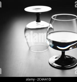 Two glasses on a black leg, one with water, the second turned upside down, against a dark background. Copyspace. Stock Photo