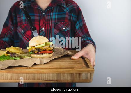 Young Man holding wooden cutting board with vegan burger and potato chips, wearing a vintage plaid shirt on white background. Vegan diet,vegetarian re Stock Photo