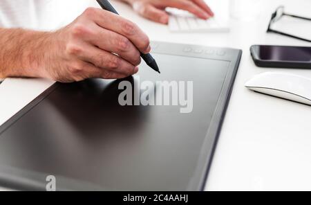 close-up of person using digital drawing tablet and stylus on white office desk Stock Photo