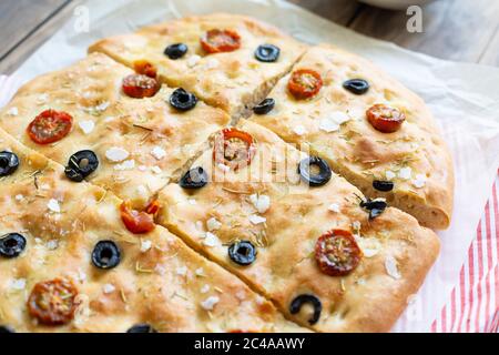 Homemade focaccia with black olives, cherry tomatoes, rosemary, flake salt and olive oil on baking paper Stock Photo