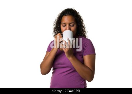 Young mixed race woman in purple shirt drinking a hot liquid from a black and white cup isolated with a white background Stock Photo