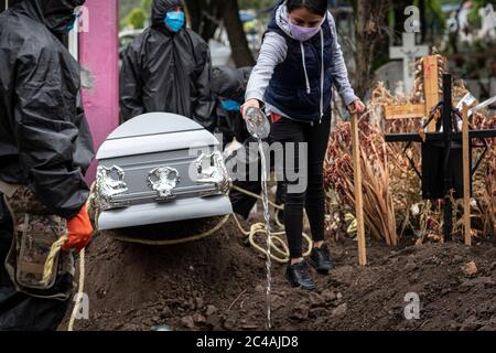 Mexiko Stadt, Mexico. 24th June, 2020. A woman wearing a face mask pours holy water into a grave during the funeral of a Covid 19 death victim at the San Isidro cemetery. Several Latin American countries are currently among the hot spots of the global pandemic - almost four months after the first cases were recorded in the region. According to official figures, 196,847 people have tested positive for Covid-19. At least 24,324 people are reported to have died from the coronavirus. Mexico has the second highest death rate in Latin America Credit: Jacky Muniello/dpa/Alamy Live News Stock Photo