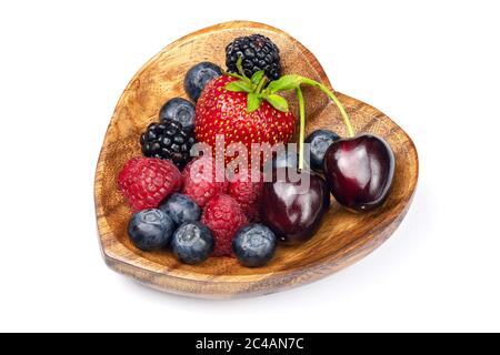 Fresh different berries in wooden bowl in the shape of heart isolated on white background. Full depth of field with clipping path. Stock Photo