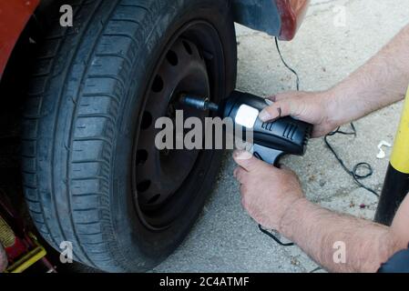 Mechanic changing wheel on car with impact wrench,  man with electric screwdriver changing tire on street close up Stock Photo