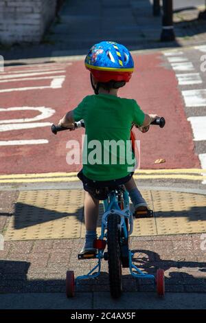 A small boy wearing a cycle helmet riding a bike with stabilisers about to cross a road Stock Photo