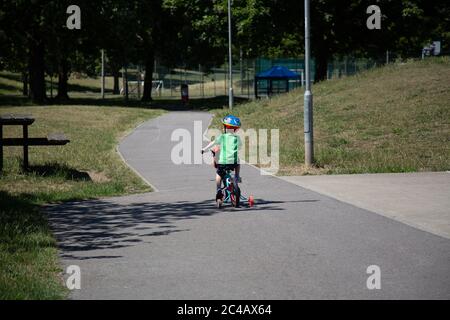 a small boy riding a bike with stabilisers through a park alone Stock Photo