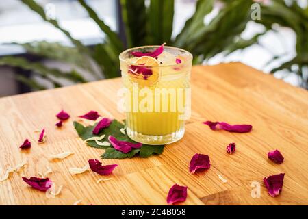 A refreshing citrus cocktail with ice in a rocks glass decorated with a dry orange slice and rose petals Stock Photo