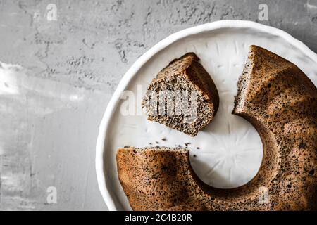 A close-up of a poppy seed bundt cake on white ceramic plate on grey background, top view photo Stock Photo