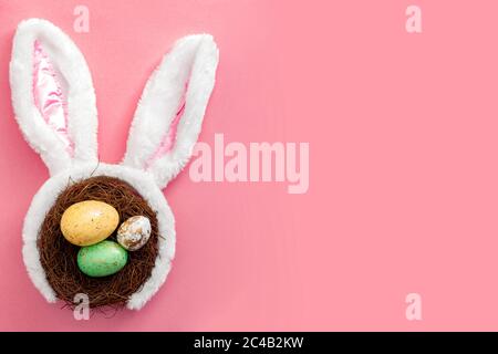 Happy Easter and spring meme concept with adorable bunny ears on a bird nest with colorful eggs against a bright pink background with copy space Stock Photo
