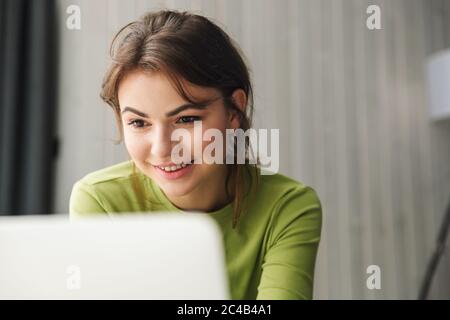Photo closeup of joyful brunette beautiful woman using laptop and smiling in cozy room at home Stock Photo
