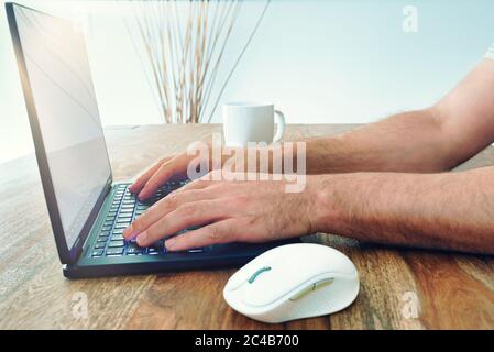 low angle view of man using laptop computer on wooden table with bright sunlight coming through window Stock Photo