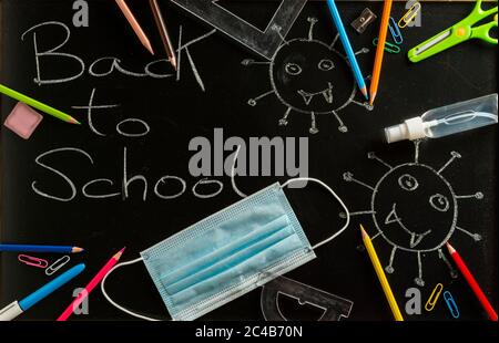 Various school supplies, face mask and hydroalcoholic gel on blackboard. Back to school concept after the covid19 pandemic. Stock Photo