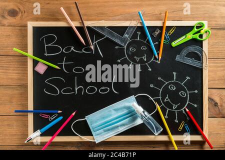 Various school supplies, face mask and hydroalcoholic gel on blackboard. Back to school concept after the covid19 pandemic. Stock Photo