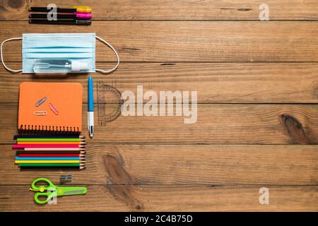 Various school supplies, face mask and hydroalcoholic gel on wooden boards. Back to school concept after the covid19 pandemic. Stock Photo