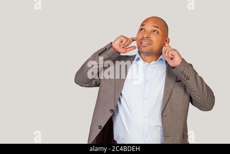 Handsome dark-skinned African-American man, a young guy with his fingers annoyed, annoyingly, not wanting to hear something, hearing loud sounds of heavy music from the apartment from above Stock Photo