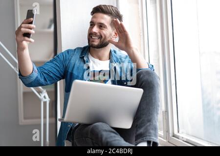 Young happy man talking video call via smartphone at home. Stock Photo