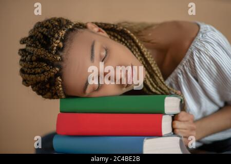 Tired young African American female sleeping on pile of books Stock Photo