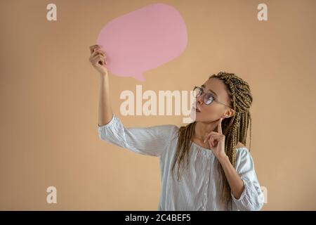Young African American female in eyeglasses holding pink dialogue cloud, touching her chin with index finger Stock Photo