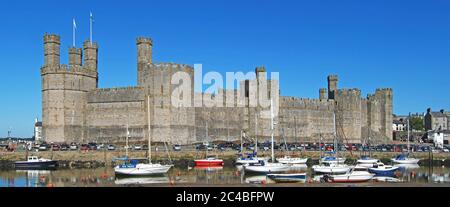 Caernarfon Castle Welsh medieval historical stone fortress building on River Seiont boats in landscape UNESCO heritage tourism Gwynedd North Wales UK Stock Photo