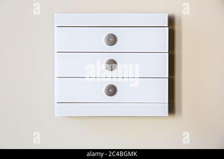 A modern white glass touch sensitive multifunctional light switch with indicators instal on a beige wall close up. Stock Photo