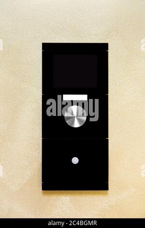 smart home control controller with a screen and buttons to control the light and temperature in the room, the device of black glass mounted on the wal Stock Photo