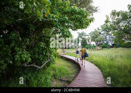 Two people, mother and teeage daughter walking on wooden path at a tented safari camp Stock Photo