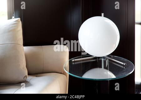 table lamp white ball on a glass round table against a black wooden wall and leather sofa, closeup of an interior lantern. Stock Photo