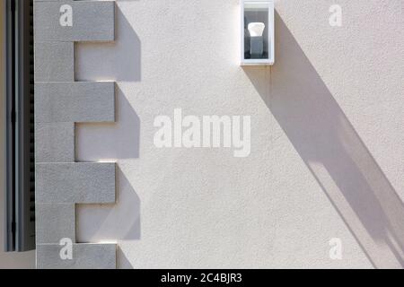 the stone wall is light beige in color with a molding on the corner of the building and a white wall lamp of square shape with a light bulb. Stock Photo