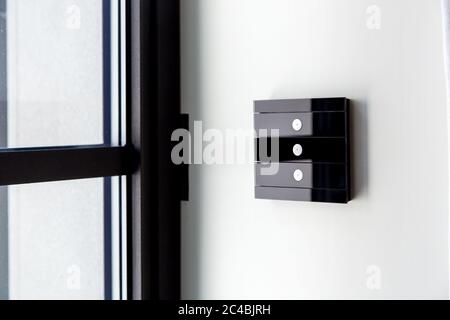 touch glass light switch of black color on a white wall near the window, close-up of the smart home control with 3 buttons. Stock Photo