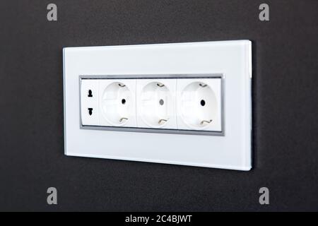 socket with plugs for standard type A plug and standard type F plug in white plastic case on a dark gray stone wall, close up side view. Stock Photo