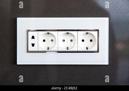 socket with plugs for standard type A plug and standard type F plug in white plastic case on a dark gray glossy stone wall. Stock Photo