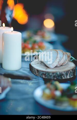 Close up of two lit candles and slices of bread on round wooden board. Stock Photo