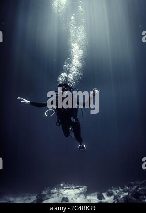 Underwater view of diver wearing wetsuit, diving goggles and oxygen cylinder, air bubbles rising. Stock Photo