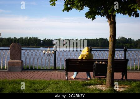a lone female figure sits on a bench near the river Stock Photo