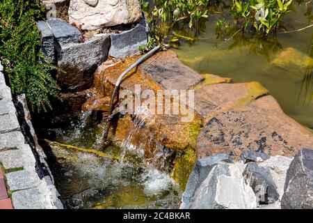 Stone cascading waterfall in an artificial pond with water in the park on a sunny day. Stock Photo