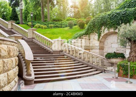 granite staircase with stone railings and balustrades with a wall rustic design in the background landscape with plants from bushes and trees and sunn Stock Photo
