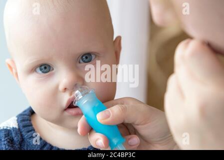 Mom cleans baby's nose from mucus using a nasal aspirator Stock Photo
