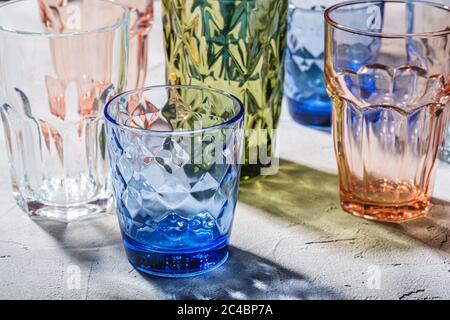 Colorful faceted and geometric drink glass, group of empty green, red, blue and transparent drinkware for beverage on stone concrete background, angle Stock Photo