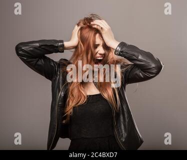 Tired from work blond hair female model with agressive emotions crying with wide opened mouth and holding head. Style clothing woman in black leather Stock Photo