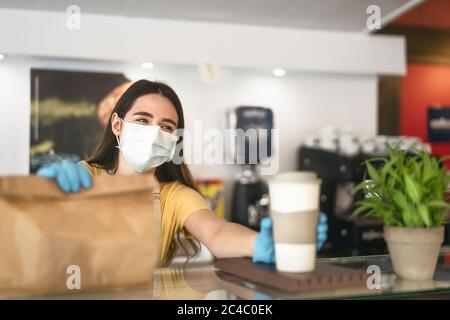 Bar owner working only with take away orders during corona virus outbreak - Young woman worker wearing face surgical mask giving meal to customers Stock Photo